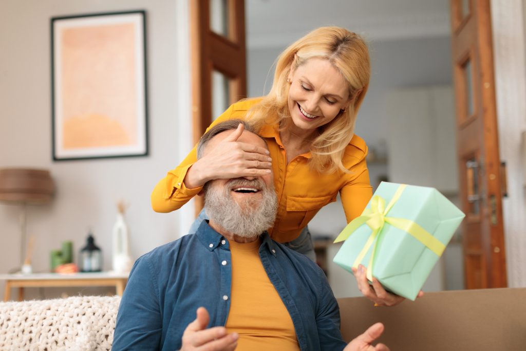 woman covering husbands eyes with hands and surprises him with wrapped gift